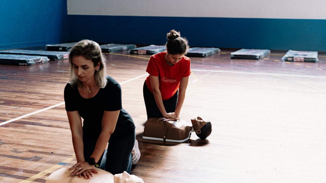 Two women learn CPR techniques on mannequins during a first aid training session.